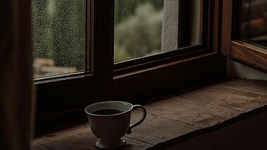 Eine Tasse Kaffee auf einem Fensterbrett, auf der Scheibe Regentropfen