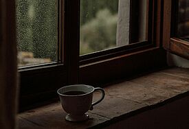 Eine Tasse Kaffee auf einem Fensterbrett, auf der Scheibe Regentropfen