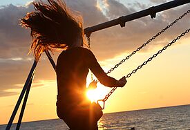 Frau im Sonnenuntergang auf einer Schaukel 