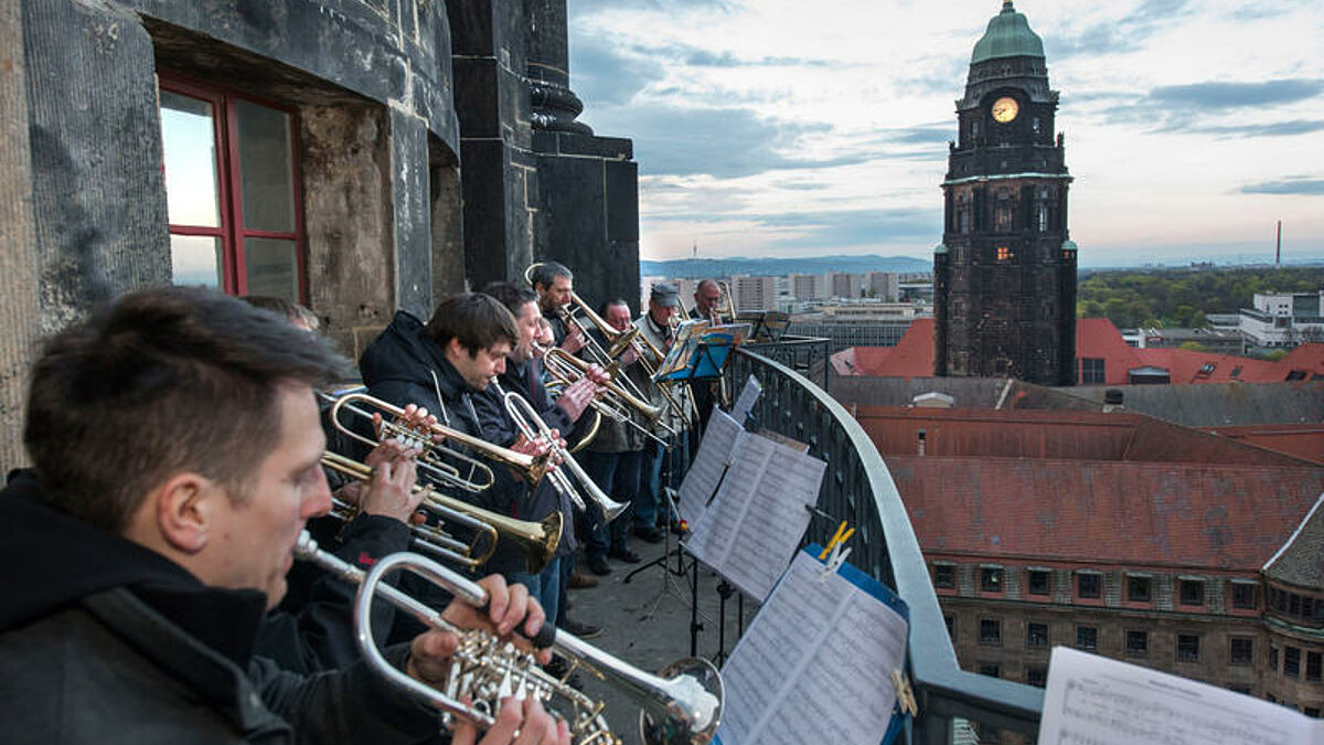 Ein Posaunenchor spiel auf dem Balkon der Kreuzkirche in Dresden, im Hintergrund ist der Rathausturm zu sehen