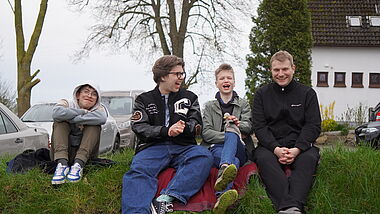 Drei Jugendliche und ein junger Mann sitzen lachend auf einem Rasenstück