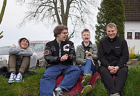 Drei Jugendliche und ein junger Mann sitzen lachend auf einem Rasenstück