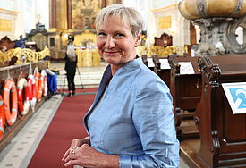 Bischöfin Kirsten Fehrs steh im Michel im Mittelgang zwischen den Kirchenbänken. Sie Trägt einen blauen Blazer.