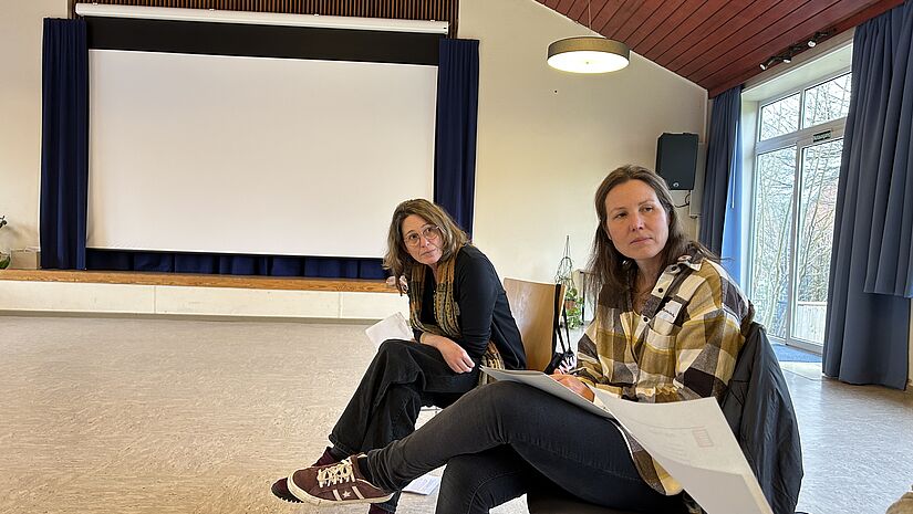 Mareike Brombacher und Johanna Bühr leiten sitzen in Saal, in dem der Workshop stattfindet.