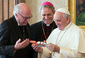 Symbolisches Geschenk: Bischof Ulrich (li.) übergibt Papst Franziskus eine Statue mit dem Logo „2017 gemeinsam unterwegs“. In der Bildmitte: Kurienerzbischof Georg Gänswein.