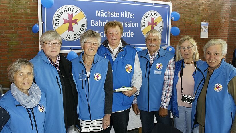 Das Team vor dem Banner der Bahnhofsmission in blauen Westen