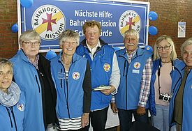 70 Jahre Bahnhofsmission in Eckernförde Das Team vor dem Banner der Bahnhofsmission in blauen Westen