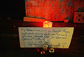 Schild mit der Bitte um Kleingeld vor Windlicht und Weihnachtskugeln