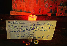 Schild mit der Bitte um Kleingeld vor Windlicht und Weihnachtskugeln