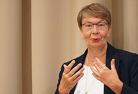 Landesbischöfin Kristina Kühnbaum-Schmidt gestikuliert mit ihrern Händen. Sie sitzt vor einem Vorhang in beige.