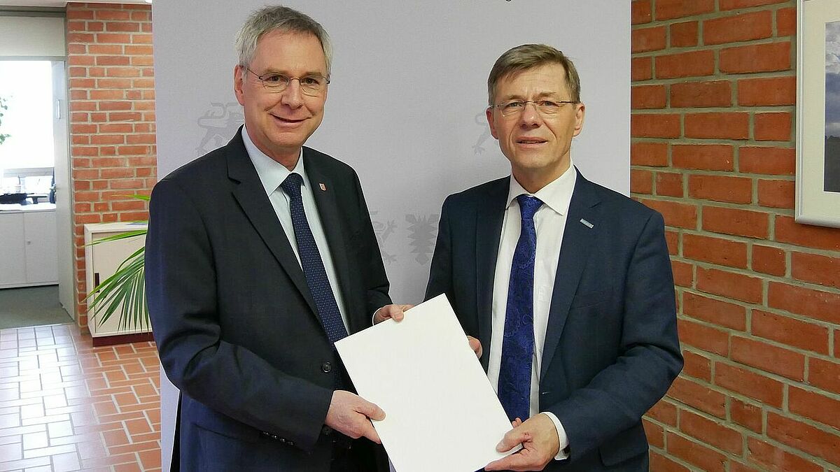 Innenstaatssekretär Torsten Geerdts (l.) übergibt Landespastor Heiko Naß den Bewilligungsbescheid.