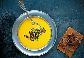 Im Bild zu sehen ist ein Teller Kürbis-Suppe neben zwei Stückchen geröstetem Brot, die als Sterne ausgestochen sind.