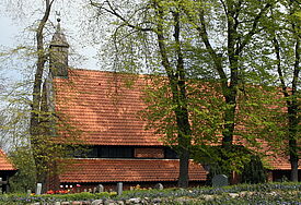 Blick auf die Kirche in Waase. Das rote Dach leuchtet durch die Kronen der Bäume, die die Kirche umgeben.