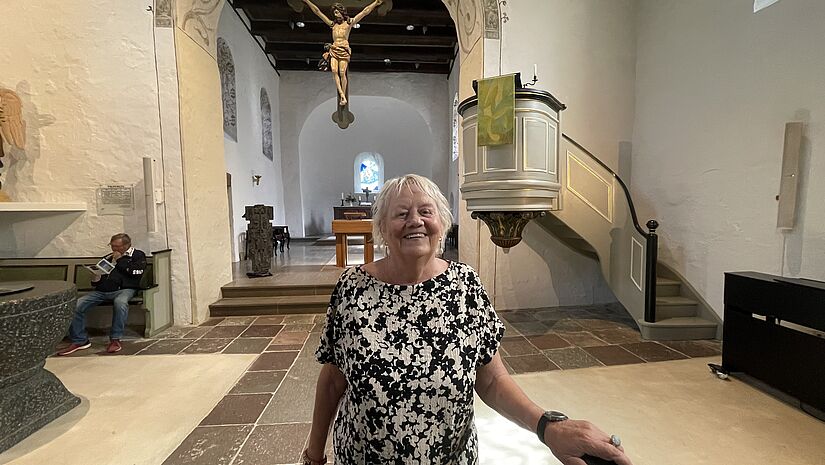 eine ältere Dame steht im Kirchenschiff der Ratekauer Kirche. Im Hintergrund der Chor mit dem Altar. 
