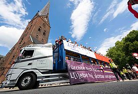 Ein großer CSD-Truck mit Bannern fährt an einem Kirchturm in Hamburg vorbei
