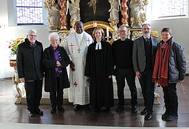 Eine Gruppe Menschen steht in der Kirche in Heide vor dem Altar, von draußen scheint das Tageslicht herein