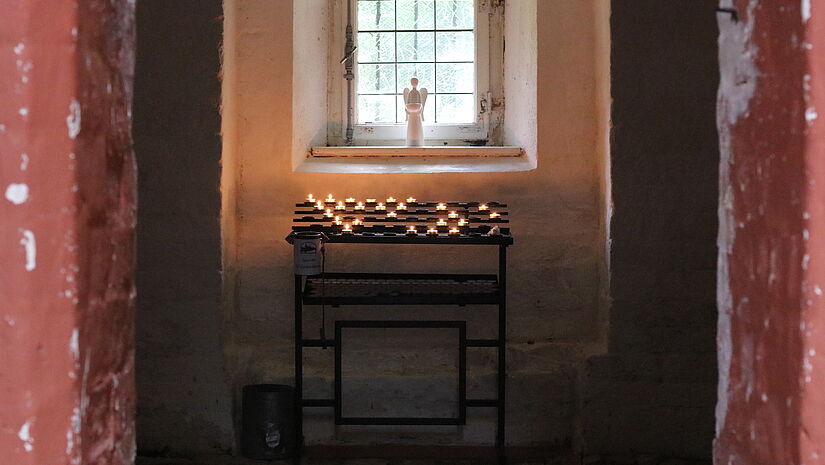 Blick in die Sakristei. Ein Engelsfigur steht im Fenster. Darunter brennen viele Kerzen.