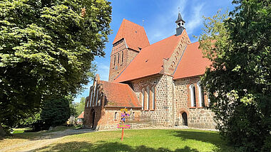 Eine alte Feldsteinkirche umgeben von großen Bäumen und Rasenflächen