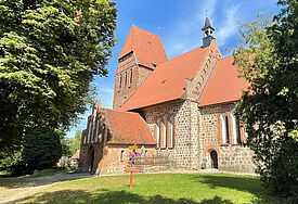 Eine alte Feldsteinkirche umgeben von großen Bäumen und Rasenflächen