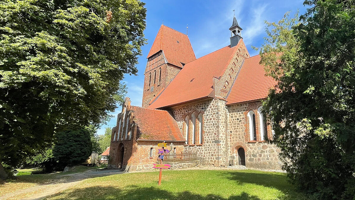 Bunte Wegweiser vor der Kirche von Recknitz sind Hinweise auf das Projekt Kultur.Feldstein.Kirche. An den Veranstaltungswochenenden füllen zahlreiche Menschen das einladende Gelände rund um die Kirche mit Leben und guter Laune. 