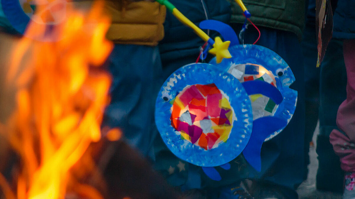 Kinder mit ihren gebastelten Laternen stehen am Martinstag am Lagerfeuer zusammen.