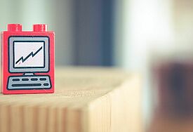 Ein roter Legostein mit Computeraufdruck steht auf einem hellen Holztisch.