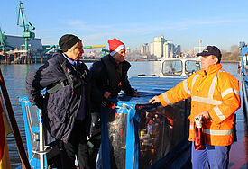 Christel Zeidler und Seemannspastor Matthias Ristau überreichen zu Nikolaus einen süßen Gruß an Binnenschiffer Darius Giergowski (rechts) im Hamburger Hafen.