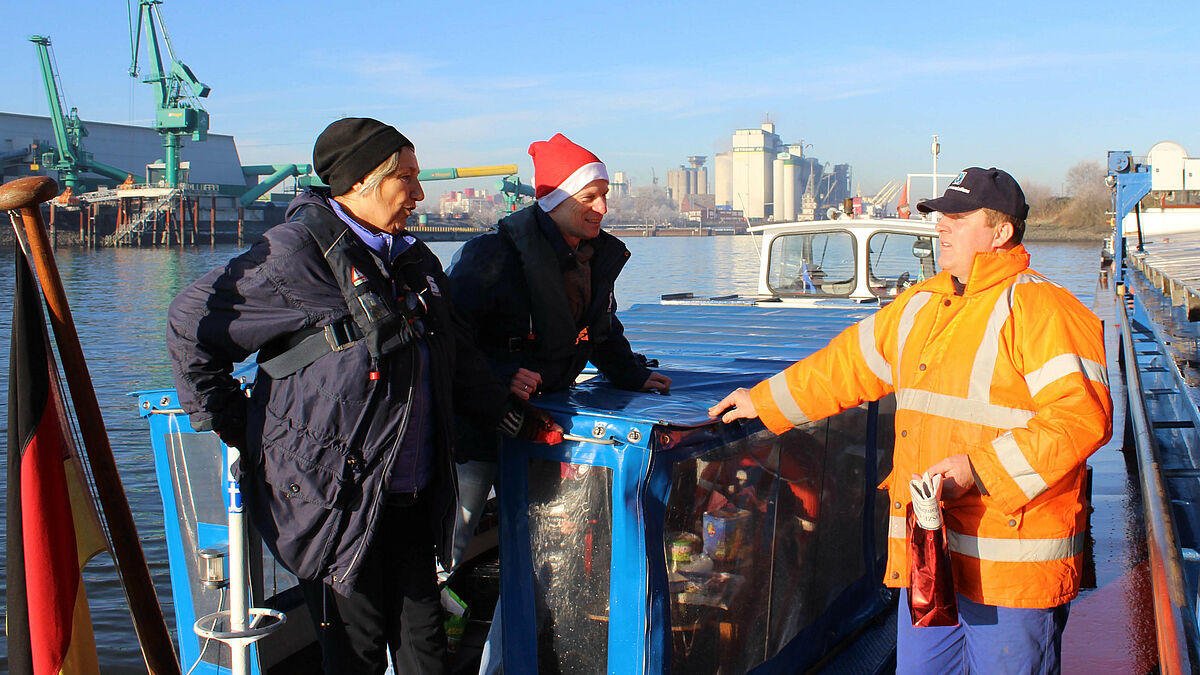 Christel Zeidler und Seemannspastor Matthias Ristau überreichen zu Nikolaus einen süßen Gruß an Binnenschiffer Darius Giergowski (rechts) im Hamburger Hafen.
