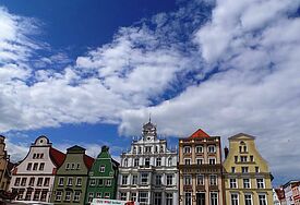 Historische Gebäude, farbig gestrichen, eng aneinander stehend, darüber der Himmel mit zarten Wolken