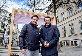 Wilko Teifke (Kirchenkreis Altholstein, v.l.) und Daniel Mourkojannis (Nordkirche) vor dem Tor in der Kieler Fußgängerzone, das zum Europäischen Stationenweg einlädt.