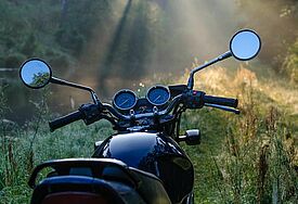 Schwarzes Motorrad morgens im Wald, rundherum Licht fällt durch die Bäume