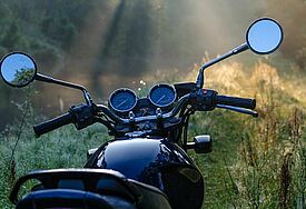Schwarzes Motorrad morgens im Wald, rundherum Licht fällt durch die Bäume