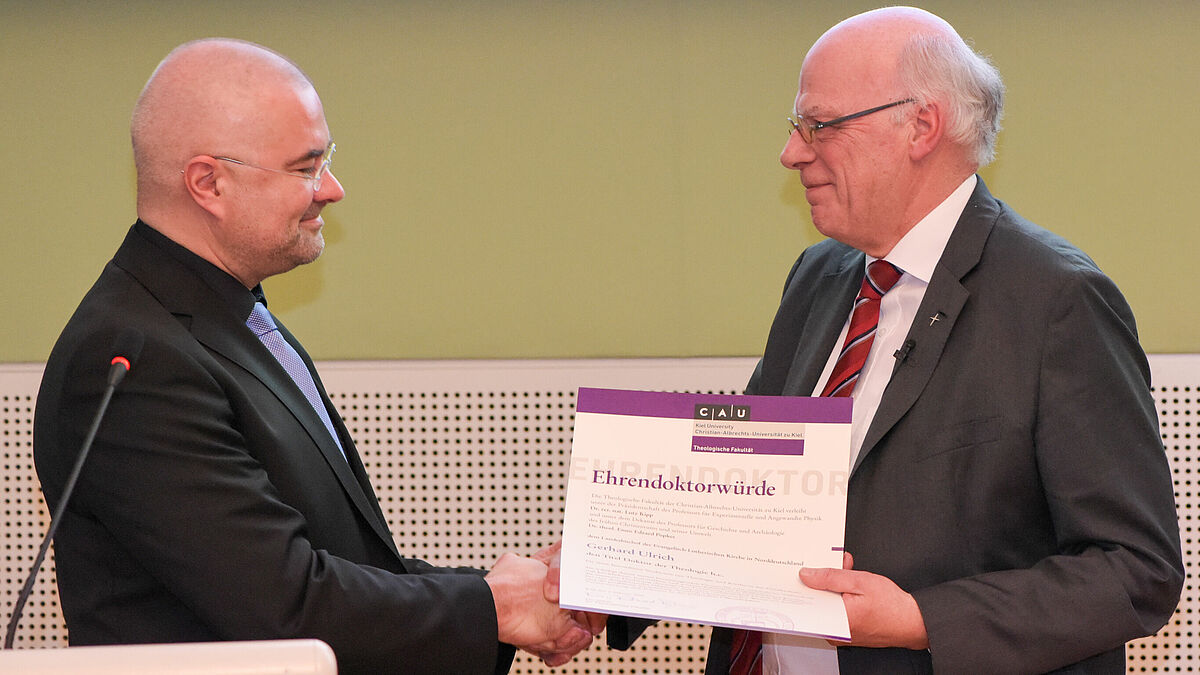 Landesbischof Gerhard Ulrich (r.) bekommt die Ehrendoktorwürde von Prof. Dr. Enno Edzard Popkes überreicht.