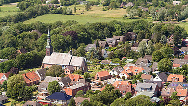 Luftaufnahme der Kirche in Tating mit umliegenden Häusern und dem Friedhof.