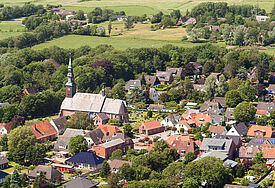 Luftaufnahme der Kirche in Tating mit umliegenden Häusern und dem Friedhof.