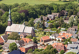 Luftaufnahme der Kirche in Tating mit umliegenden Häusern und dem Friedhof.