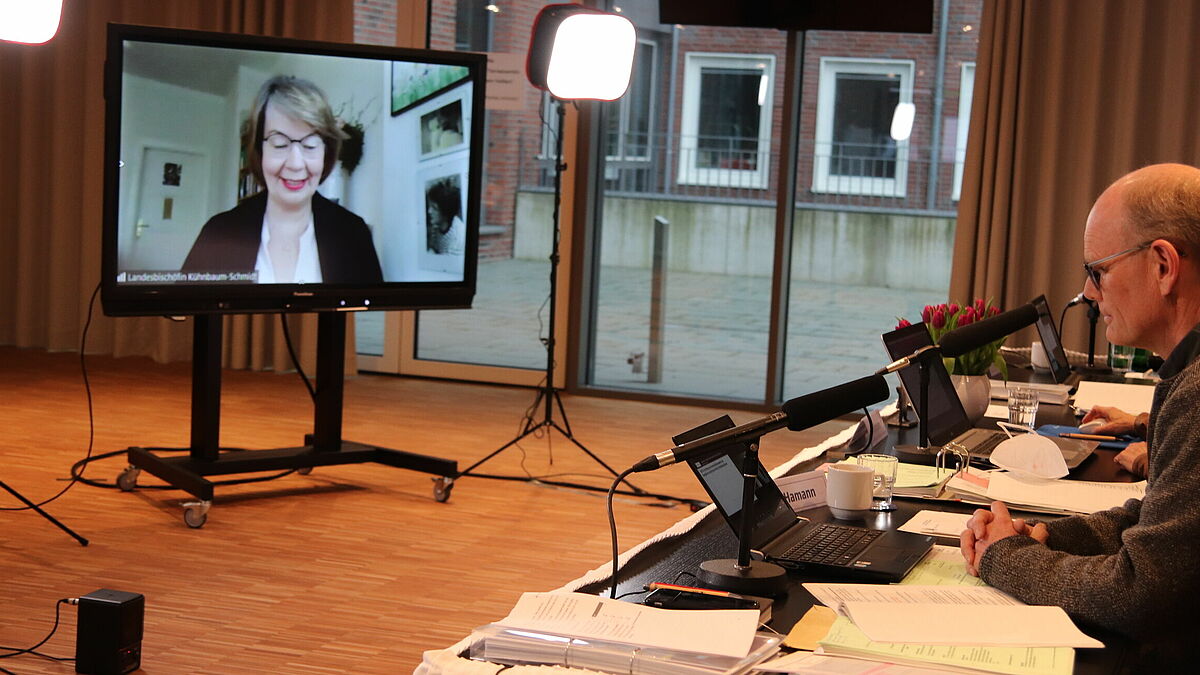 Blick vom Präsidiumstisch zum Monitor: Landesbischöfin Kühnbaum-Schmidt spricht über das zu gründende Kommunikationswerk