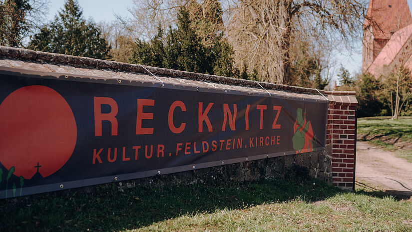 Ein Banner mit dem Schriftzug "Recknitz" ist an einer Kirchenmauer besfestigt.