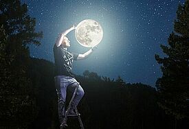 Mann steht auf einer Leiter im Dunklen und umfasst den Vollmond