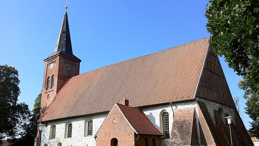 Seitenansicht der Kirche, die weiß verputzt ist und ein Ziegeldach trägt.