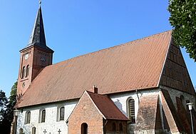 Seitenansicht der Kirche, die weiß verputzt ist und ein Ziegeldach trägt.