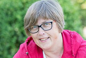 Porträt von Astrid Faehling (50), kurze Haare, Brille, rote Kapuzenjacke, im Hintergrund ist es grün.