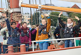 Junge Menschen an Bord des Klima-Sail Segelkschiffs winken zum Abschied