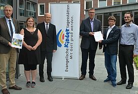 VEK-Vorsitzender Propst Sönke Funck, Kita-Mutter Jessica Nordt, Bischof Gothart Magaard und VEK-Geschäftsführer Markus Potten nehmen die Ergebnisse der Elternbefragung aus den Händen von Prof. Andreas Langer und Henning Kiani (DISW) entgegen. 