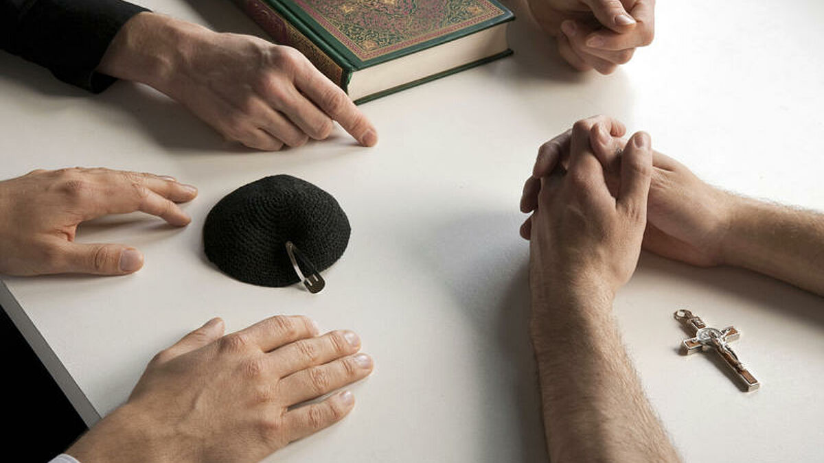 Symbole für die drei monotheistischen Weltreligionen Christentum, Judentum und Islam: Kreuz, Kipa und Koran