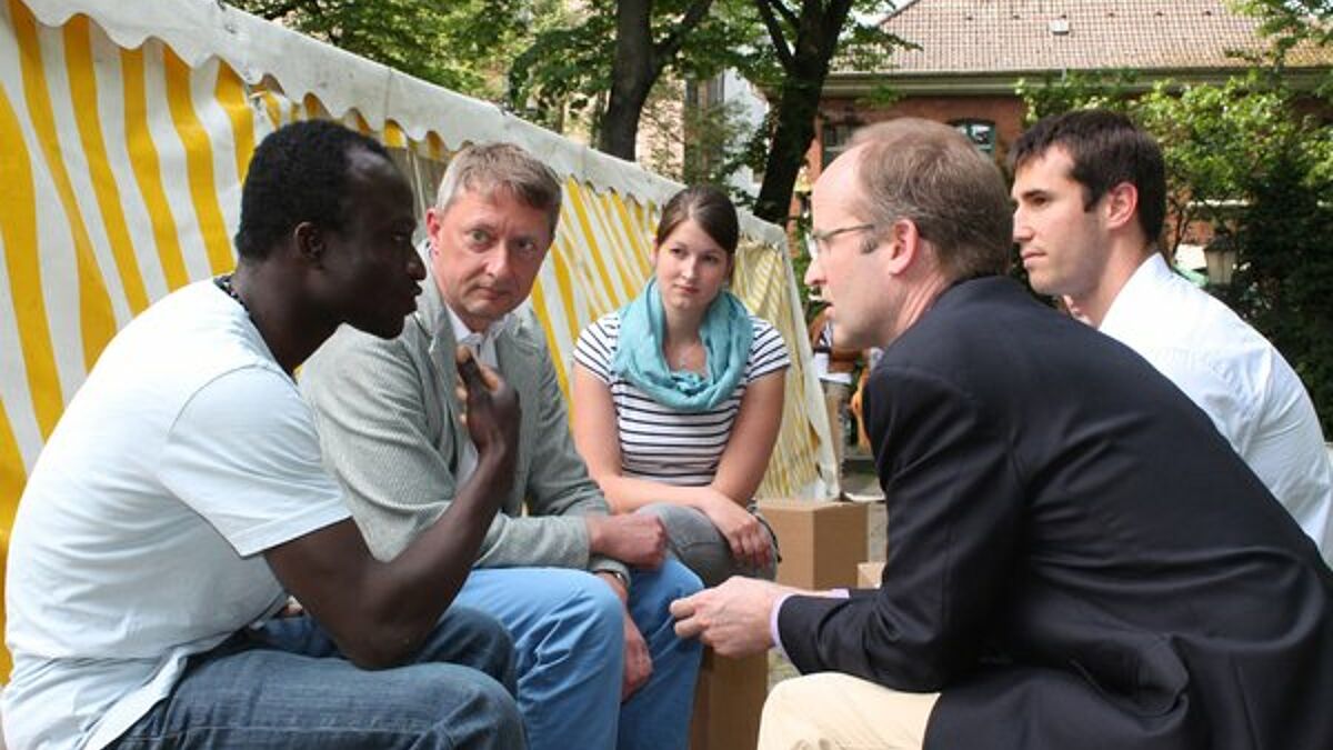 Andreas A. (li) ist einer der Sprecher der Fluechtlings-Gruppe "Lampedusa in Hamburg". Er sprach im Juni bereits mit dem amerikanischen Vize-Generalkonsul Robert Stevens (re). Mit dabei: Pastor Sieghard Wilm und Constanze Funck (Nordkirche)