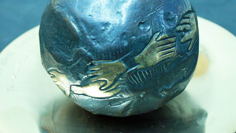 Eine Welt Bronze-Weltkugel, auf der Hände zu sehen sind, die die Kugel umfassen