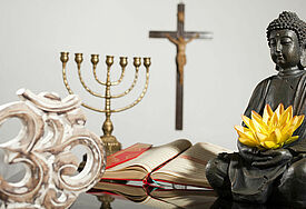Symbole der Weltreligionen: OM-Symbol für Hinduismus, Menora (siebenarmiger Leuchter) für das Judentum, Kreuz für das Christentum, Koran für den Islam und Buddhafigur für Buddhismus