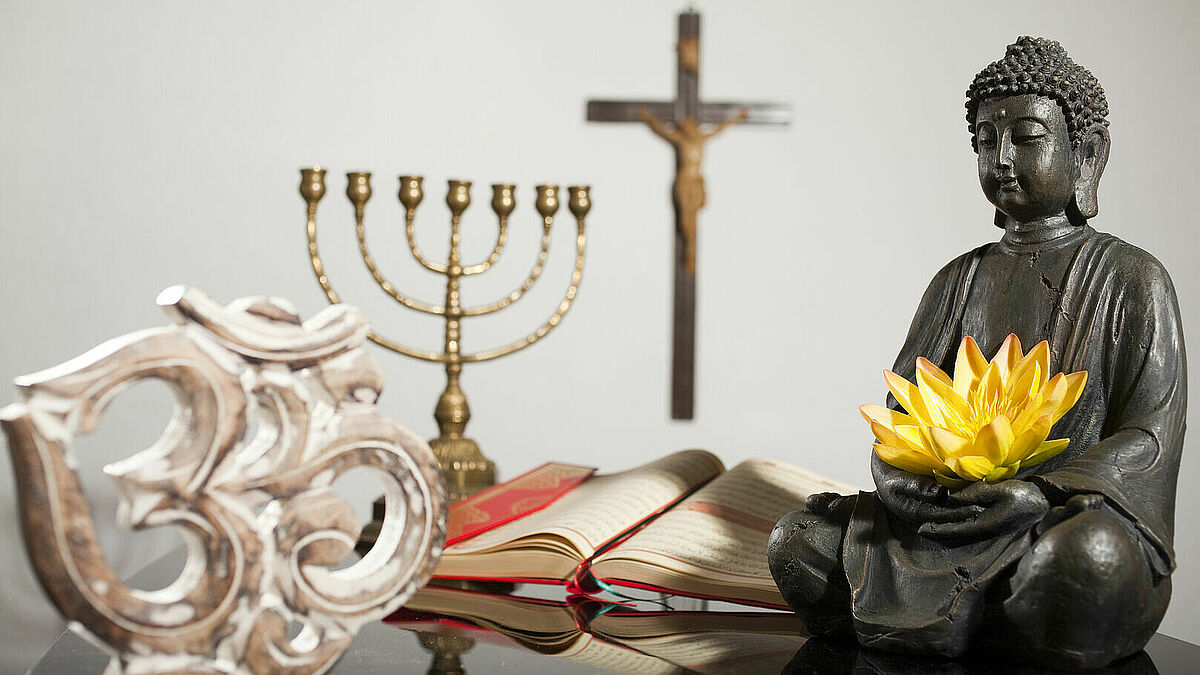 Symbole der Weltreligionen: OM-Symbol für Hinduismus, Menora (siebenarmiger Leuchter) für das Judentum, Kreuz für das Christentum, Koran für den Islam und Buddhafigur für Buddhismus