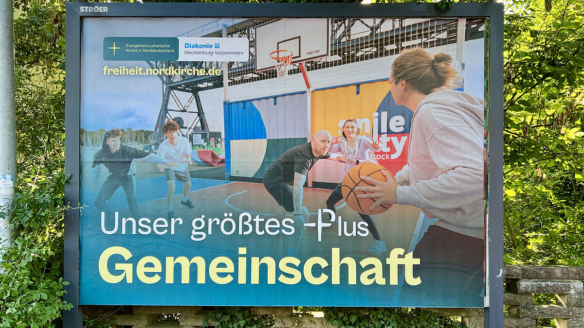 Dieses Plakat zeigt das Wertemotiv „Gemeinschaft“. Es wirbt in der Wismarschen Straße in Schwerin für "Unser größtes Plus". @Jonny Franzke / Nordkirche